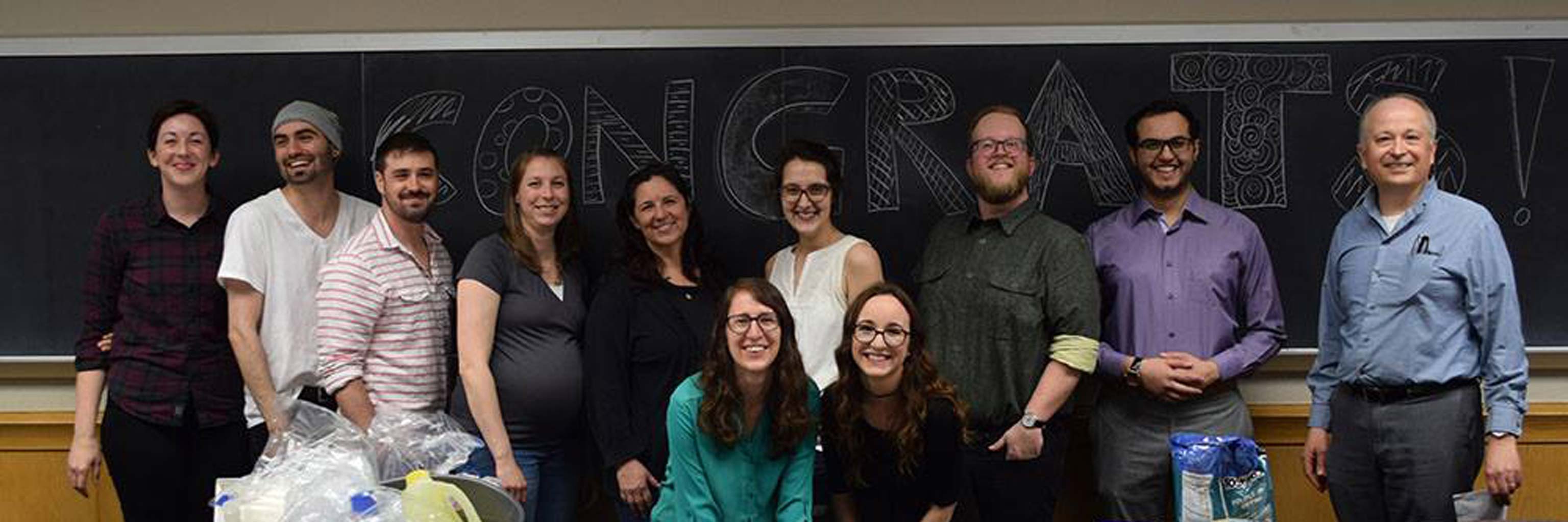 11 SLS faculty standing in front of a chalkboard that says "CONGRATS!"